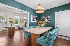 A dining area with a wooden table, teal upholstered chairs, and a hanging light fixture.