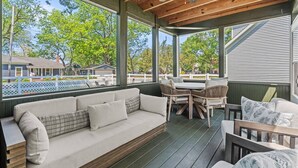 A covered porch with a sofa, dining table, and chairs, overlooking a residential area. - Renovated 1871 Chestnut House | Hot Tub & Fire Pit (Douglas)