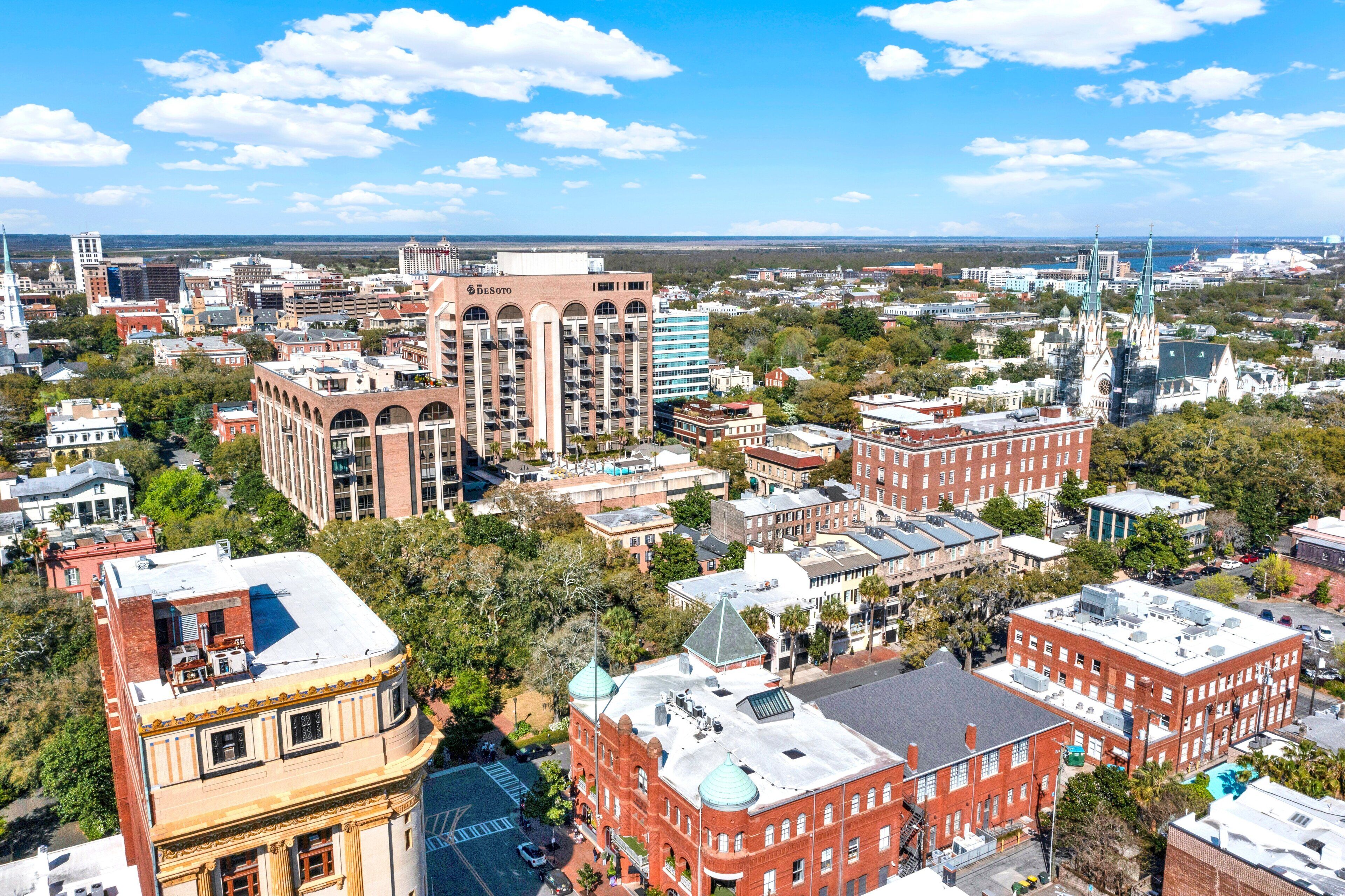 A cityscape with historic buildings, including a prominent red brick building with a dome and a modern high-rise with a green spire.