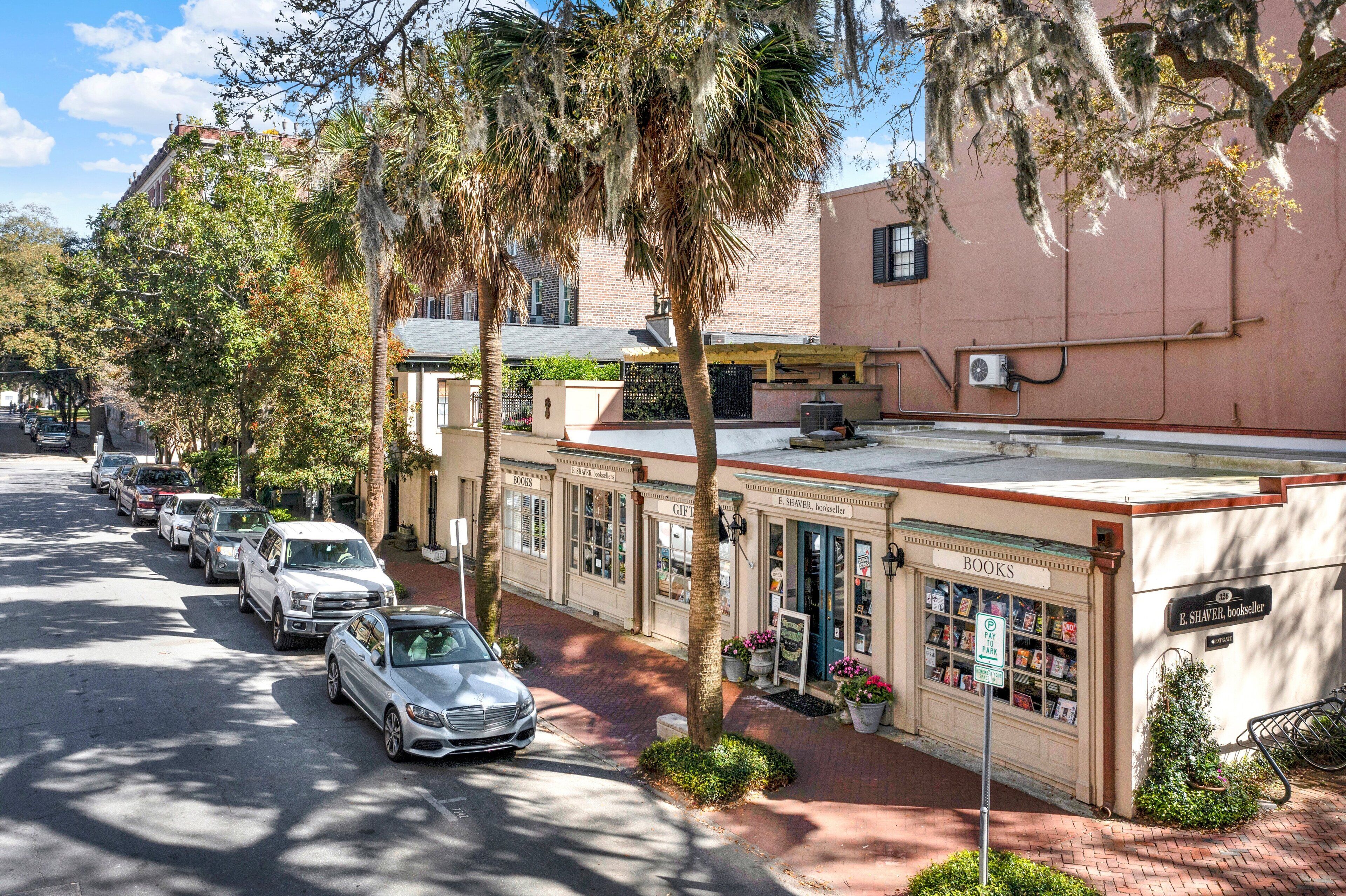 Una calle con coches aparcados y una hilera de edificios, con una librería y una tienda de regalos.