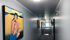 A hallway with a large painting on the left wall, a carpeted floor, and a series of doors along the right wall.