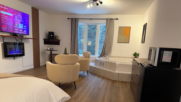 A modern hotel room with a large TV, a sofa, a desk, a bathtub, and a refrigerator.