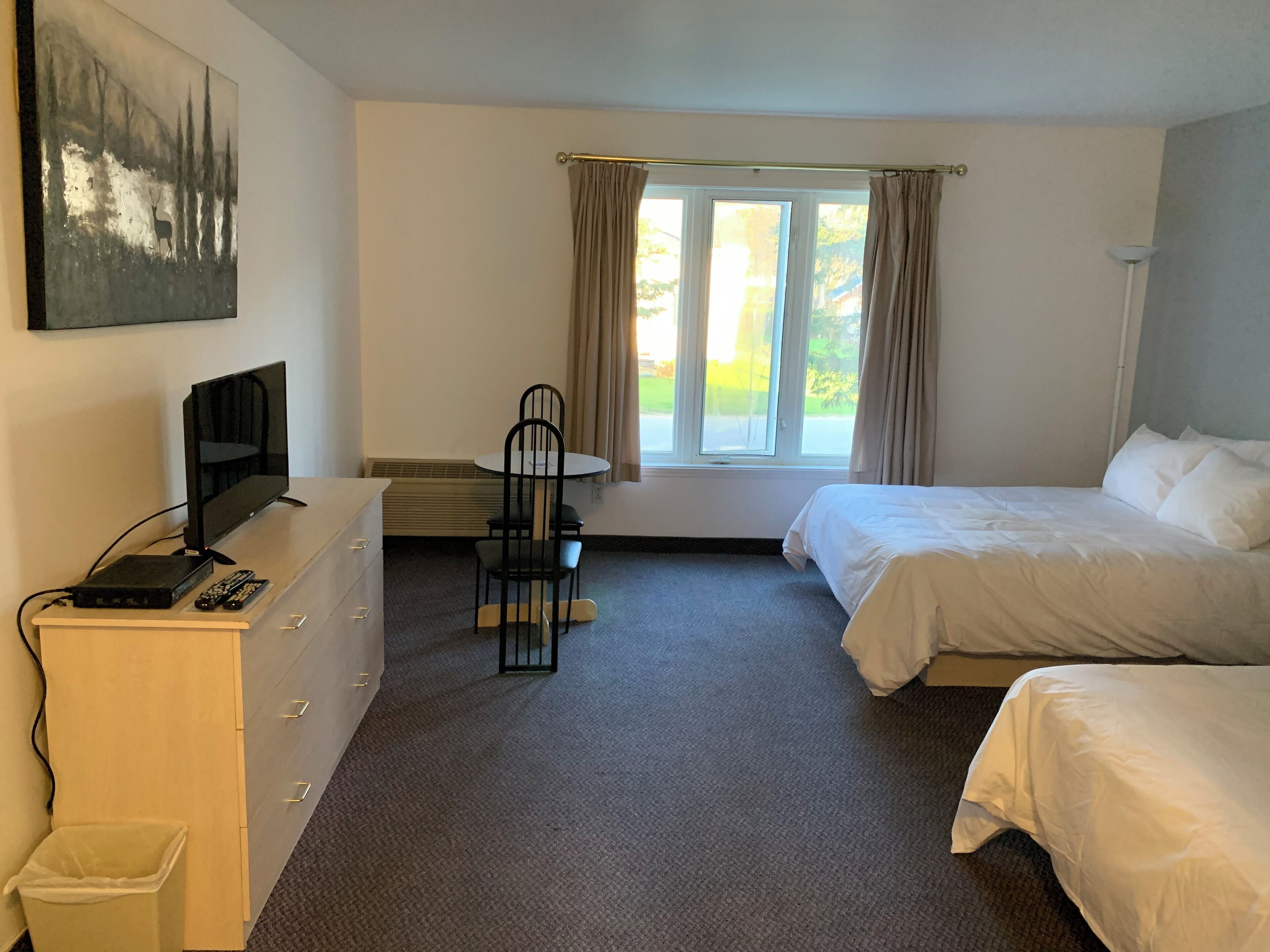 Une chambre d’hôtel avec un lit, un bureau avec une télévision, une chaise et une fenêtre avec des rideaux.