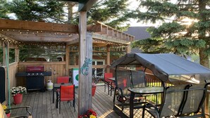 A covered outdoor deck with a barbecue area, seating, and a pergola with string lights.
