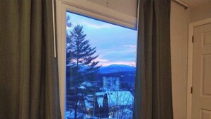 Una habitación con ventana que da a un paisaje nevado, una cama con una colcha roja y una puerta cerrada.