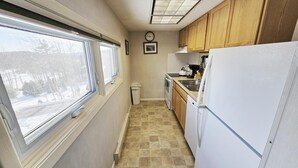 A narrow kitchen with a window, wooden cabinets, a white refrigerator, and a tiled floor. - Centrally located 2BR condo, Hot Tub&Indoor Pool (Stowe)