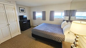 A hotel room with a bed, a dresser, a TV, two windows with curtains, and a lamp. - Centrally located 2BR condo, Hot Tub&Indoor Pool (Stowe)