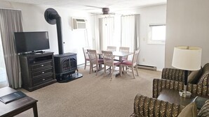 A living room with a TV, a fireplace, a dining table with chairs, and a sofa. - Centrally located 2BR condo, Hot Tub&Indoor Pool (Stowe)