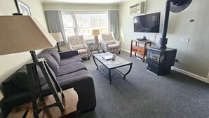 Una sala de estar con sofá, sillón y una mesa de centro. Hay una chimenea, un televisor y una lámpara.