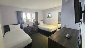 Habitación de hotel con dos camas individuales, un escritorio, un aparador, un televisor y una ventana con cortinas.