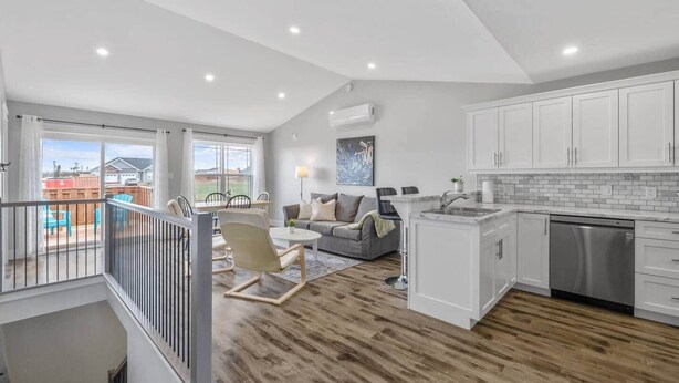 A spacious living area with a balcony, a kitchen with white cabinets, and a dining area with a table and chairs.