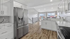 A modern kitchen with white cabinetry, a stainless steel refrigerator, a built-in oven, and a wooden floor.