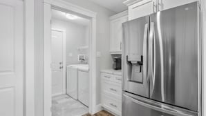 A modern kitchen with white cabinetry, a stainless steel refrigerator, and a built-in coffee maker.