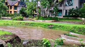 A riverside view of a modern building with a garden and a small stream. - Tree Scape Mountain View Resort (Hang Dong)