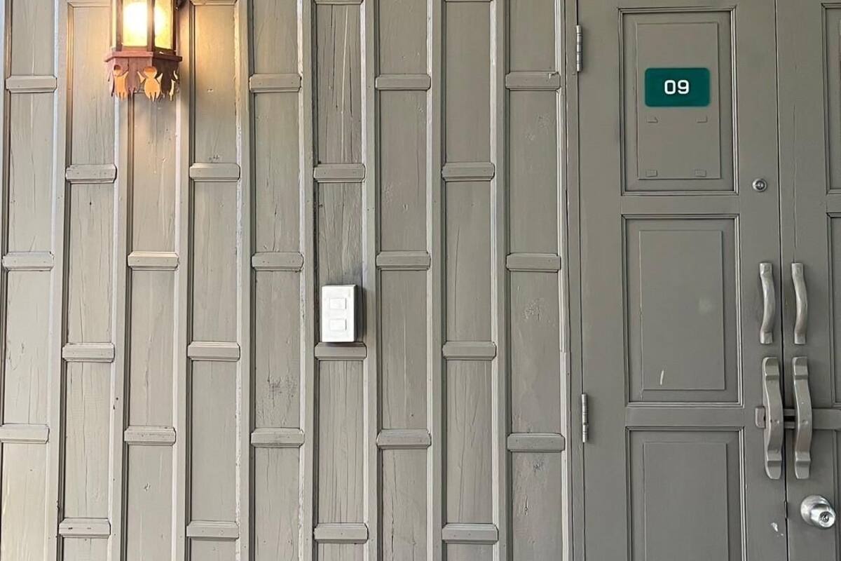 En grå dør med en grøn nummerplade med teksten "09" og en vægmonteret lampe.