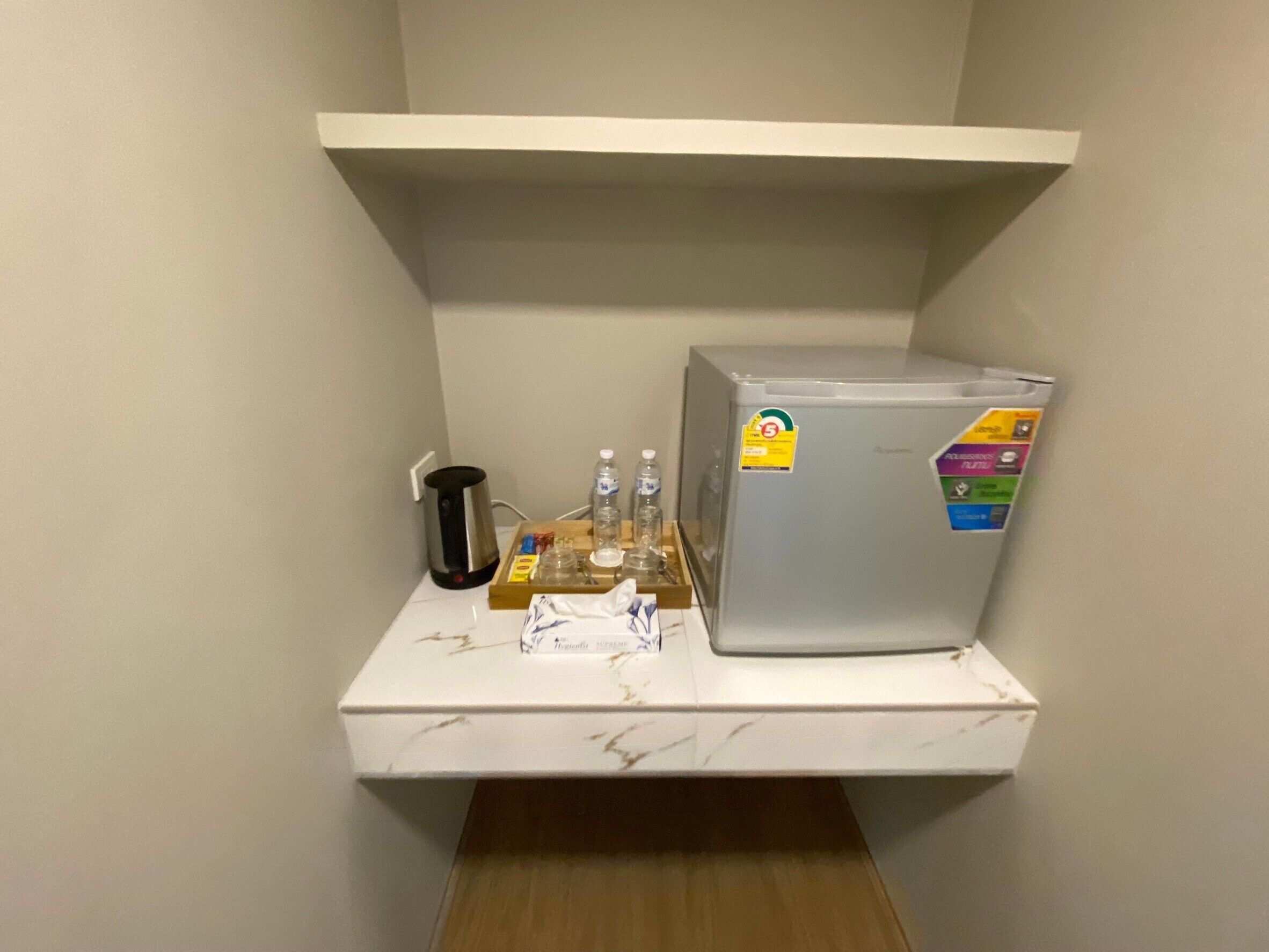A small kitchenette with a refrigerator, a coffee maker, and a water dispenser on a white countertop.