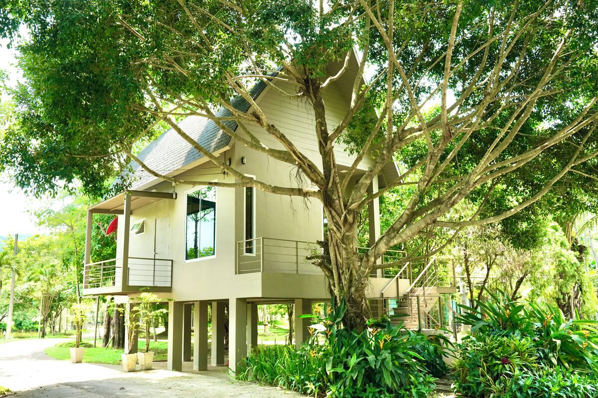 Et toetagers hus med balkon, omgivet af frodig vegetation og en velplejet have.