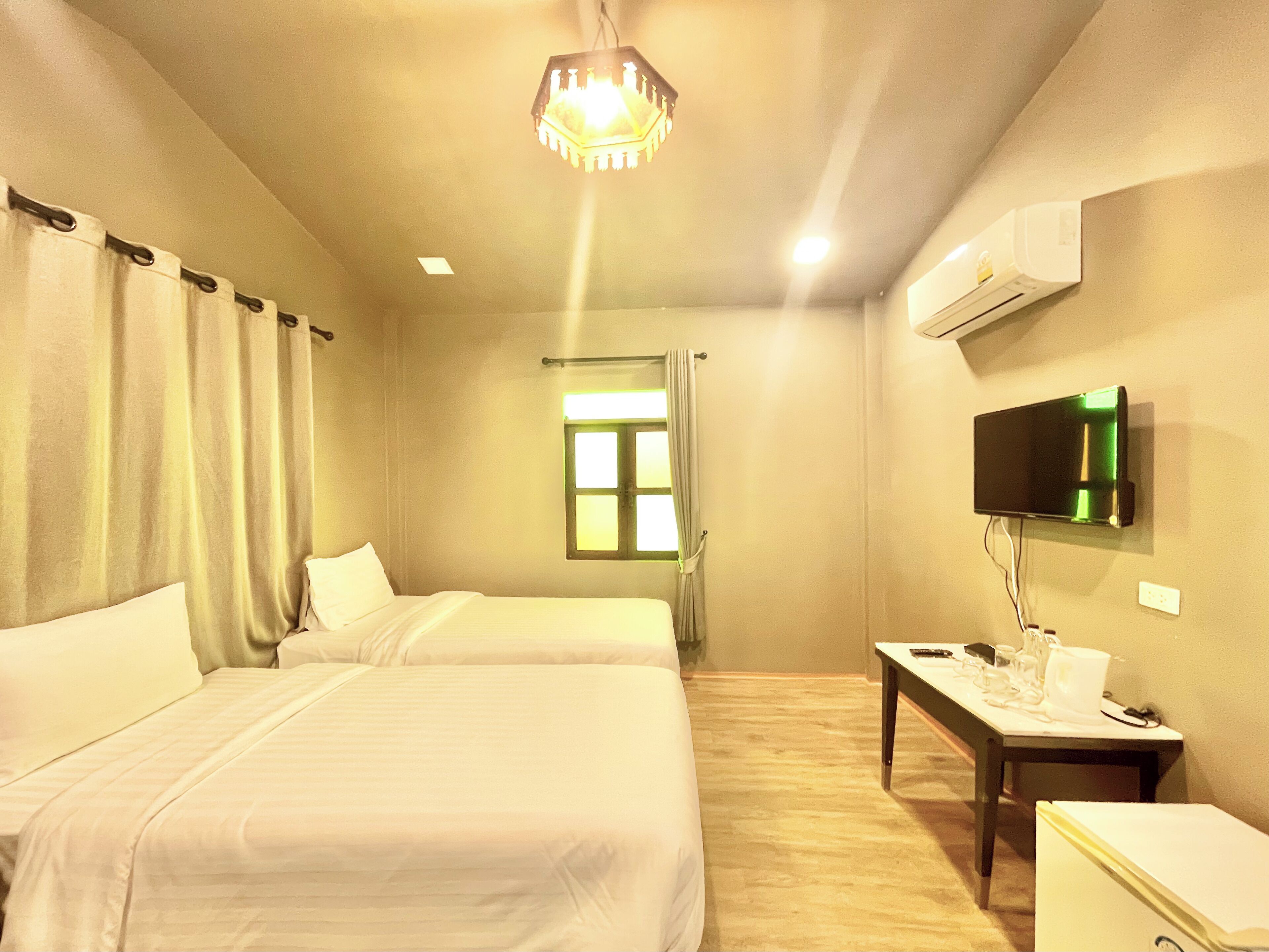A hotel room with two beds, a television mounted on the wall, and a window with curtains.