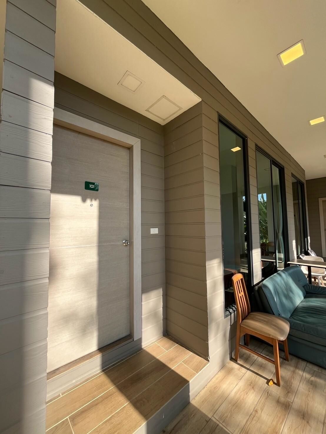 Un interior moderno con una puerta cerrada que indica '101', piso de madera y una zona de estar con un sofá azul y una silla de madera.