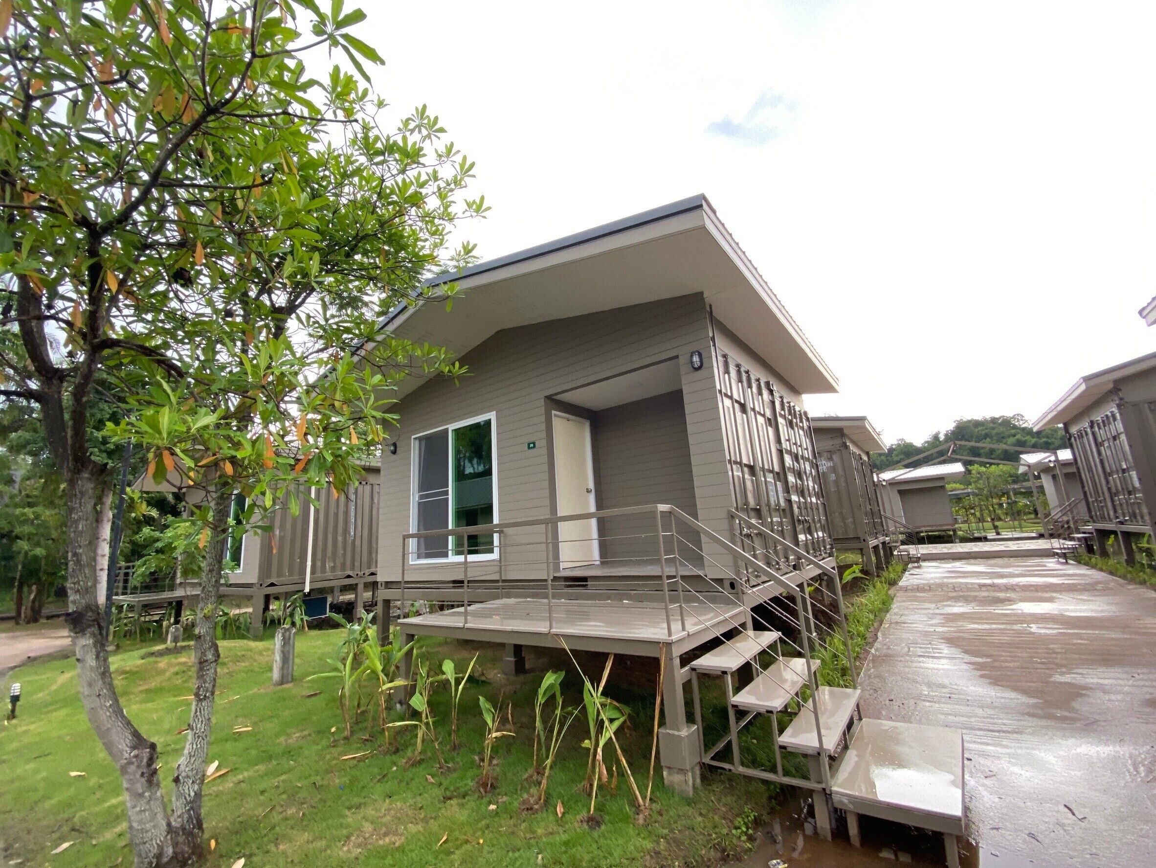 A modern building with a flat roof, a covered outdoor area with a metal staircase, and a grassy lawn with young trees.