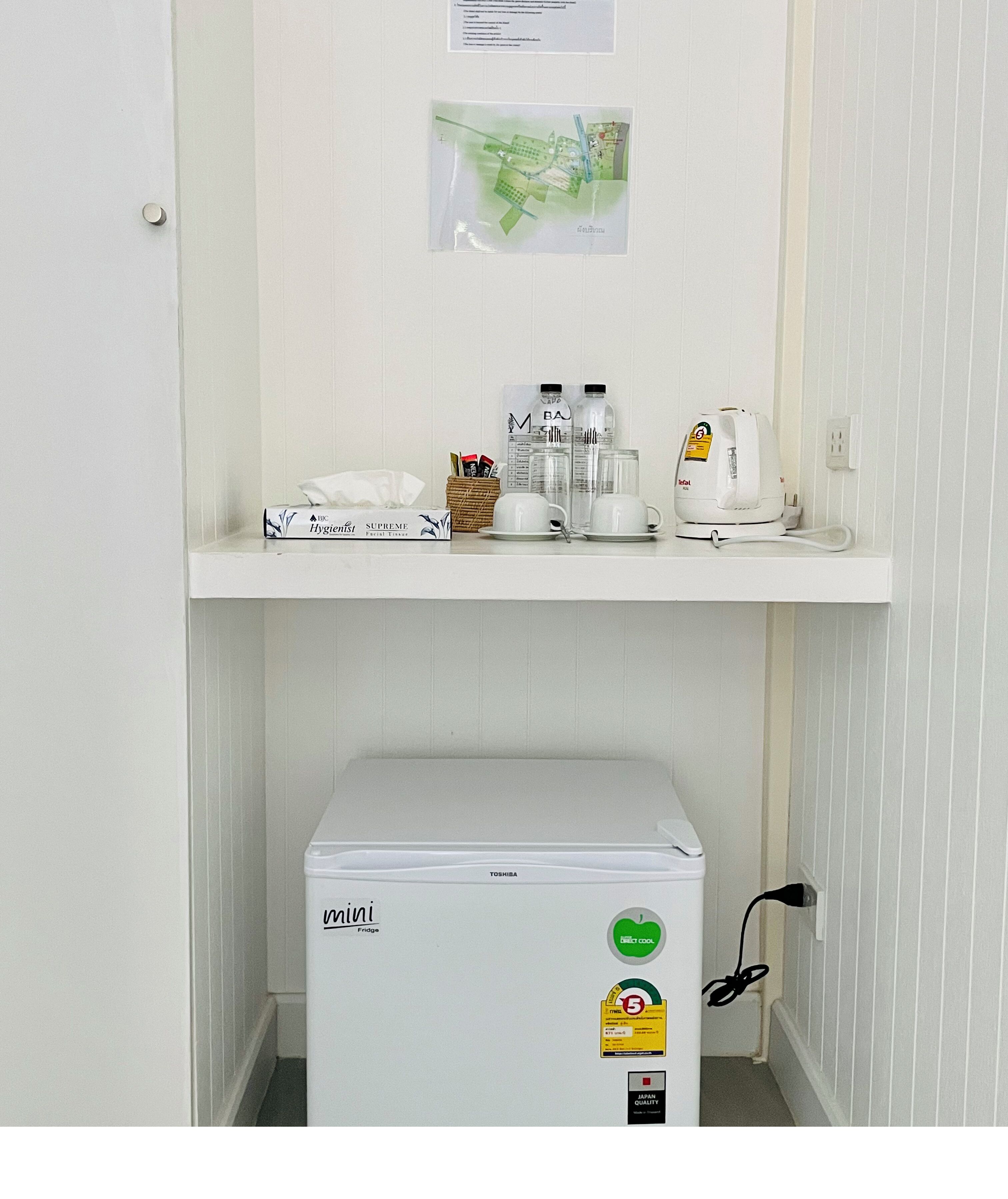 Un petit réfrigérateur, une étagère avec des articles de toilette et une carte accrochée au mur.