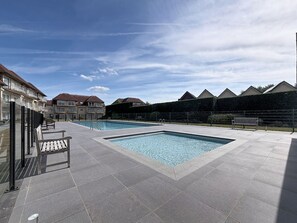 Un espace piscine doté d’une terrasse carrelée, de bancs et d’une clôture.