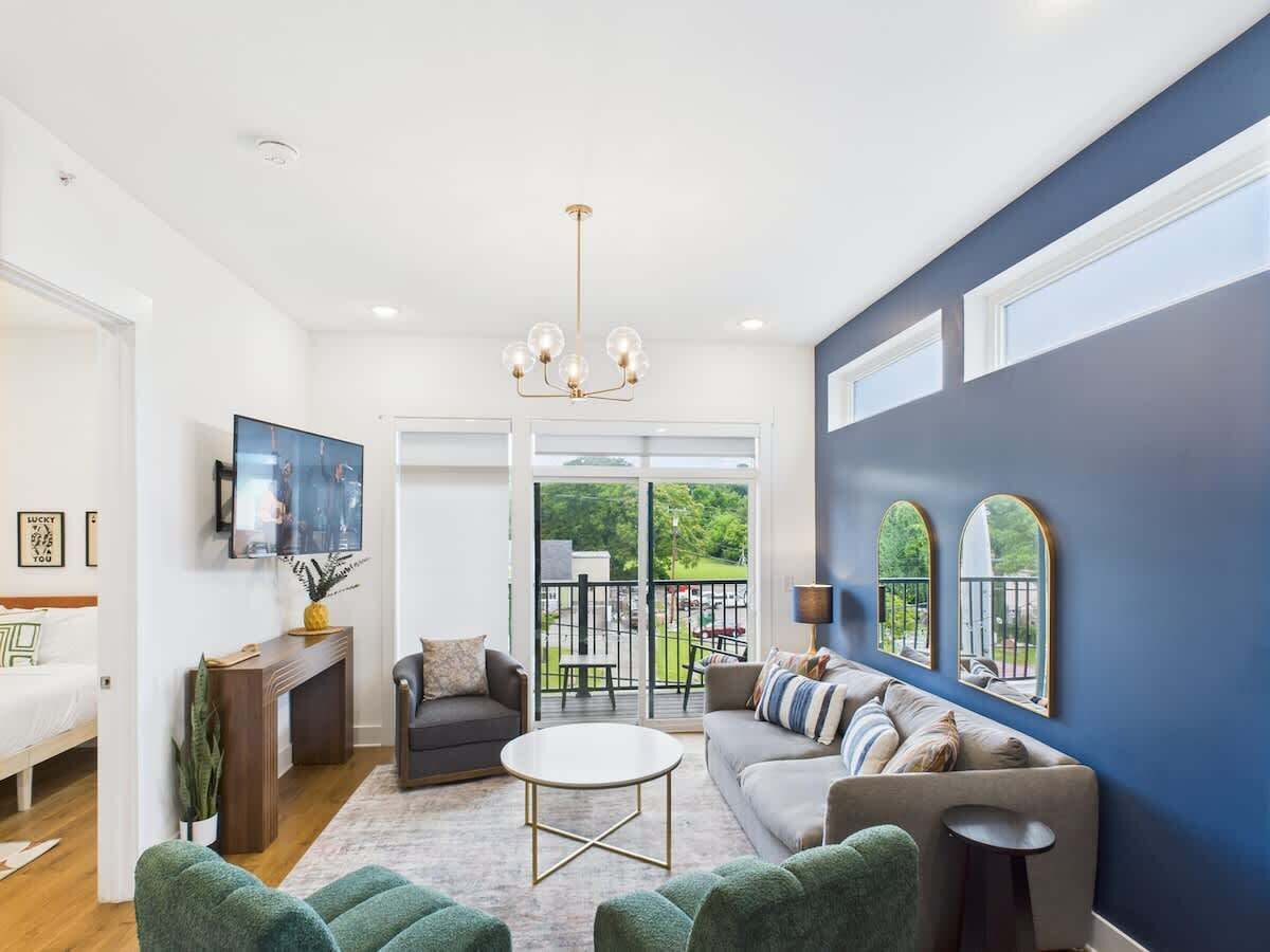 Bright open floor living space featuring a smart flat-screen TV, designer furnishings, and a private balcony entrance.