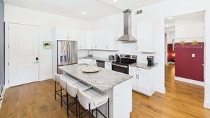 A modern kitchen with white cabinets, a central island with stools, stainless steel appliances, and a red accent wall. - Gallatin Retreat-Rooftop- Full Gym -East Nashville (Nashville)