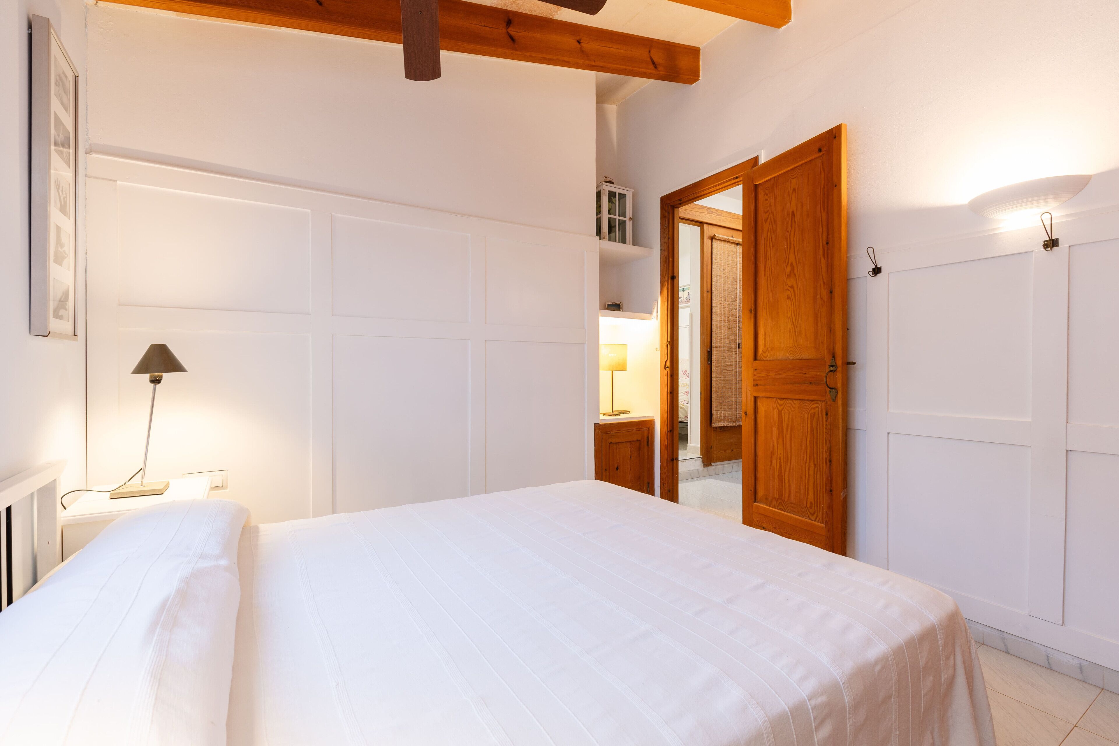 Un dormitorio con una cama grande, una lámpara de noche, una puerta de madera y un armario blanco.