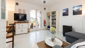 A living room with a flat-screen TV, a sofa, a glass coffee table, and a bookshelf.