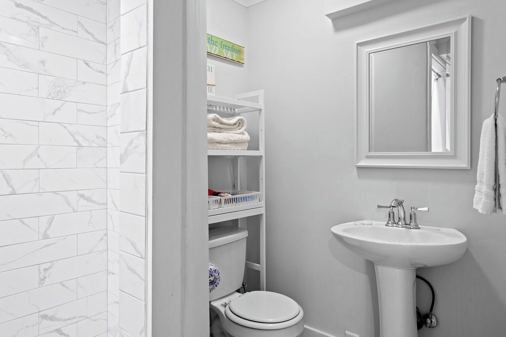 Une salle de bain avec des toilettes blanches, un lavabo blanc et un miroir au-dessus du lavabo. On y trouve une étagère avec des serviettes pliées et une pancarte au-dessus.