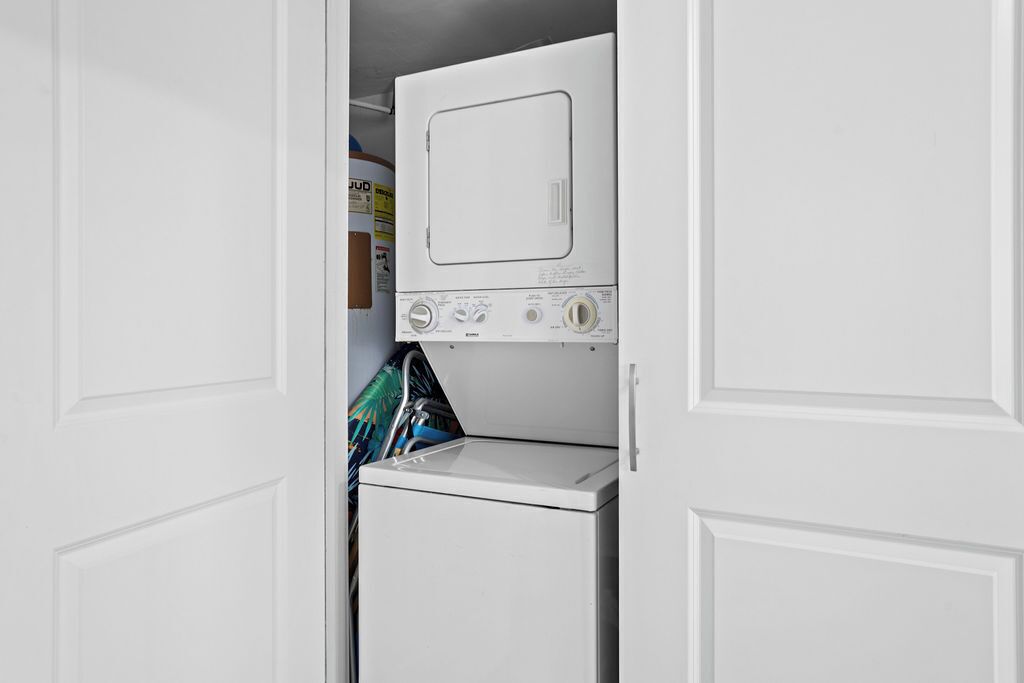 A compact laundry room with a front-loading washer and dryer, a small storage cabinet, and a door with a handle.