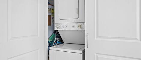 A compact laundry room with a front-loading washer and dryer, a small storage cabinet, and a door with a handle.