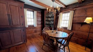 Ein Esszimmer aus Holz mit einem runden Tisch, Stühlen, einer Kandelaber und einem Regal mit Geschirr.