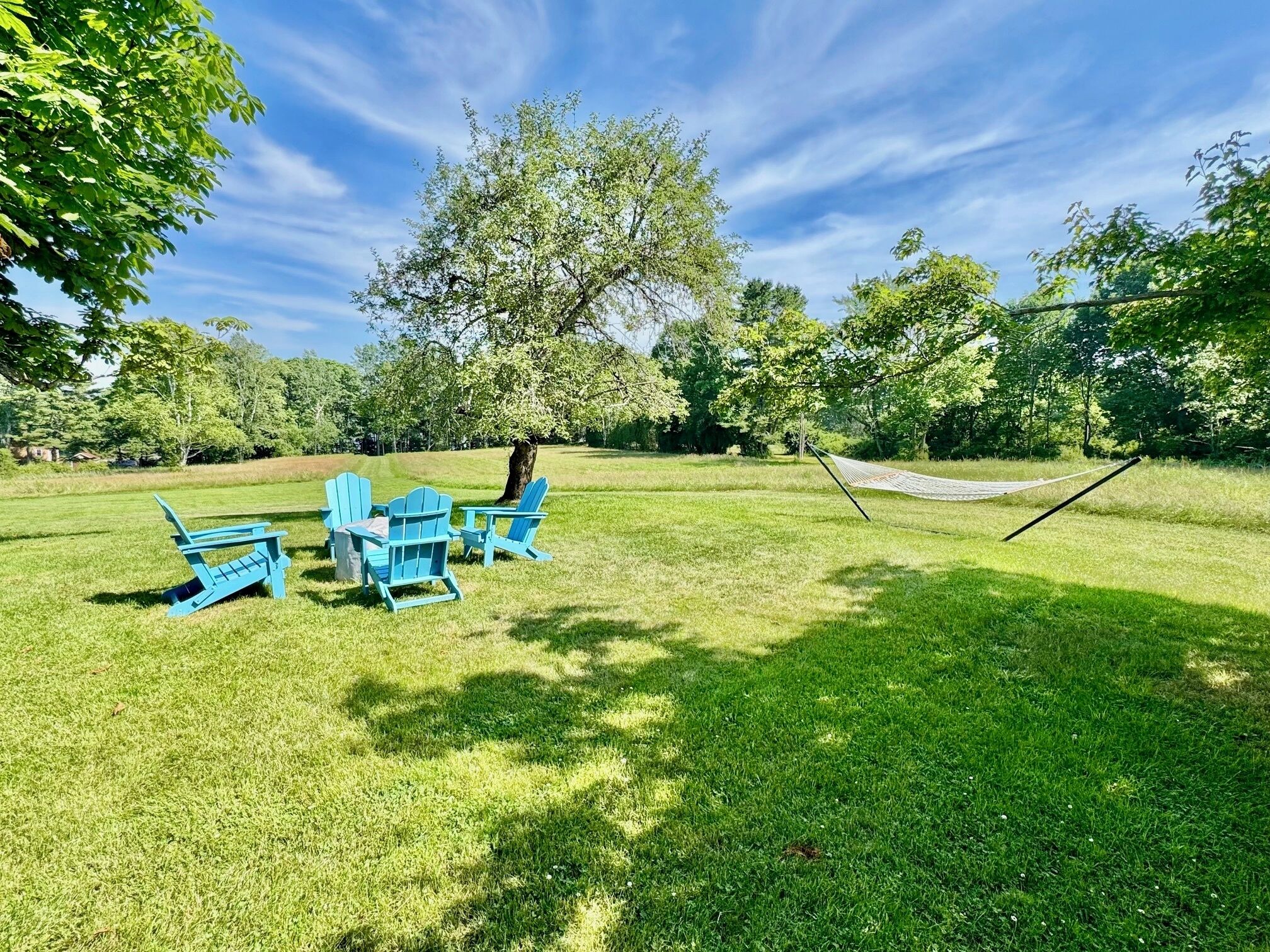 A grassy outdoor area with a hammock, a picnic table, and several Adirondack chairs.