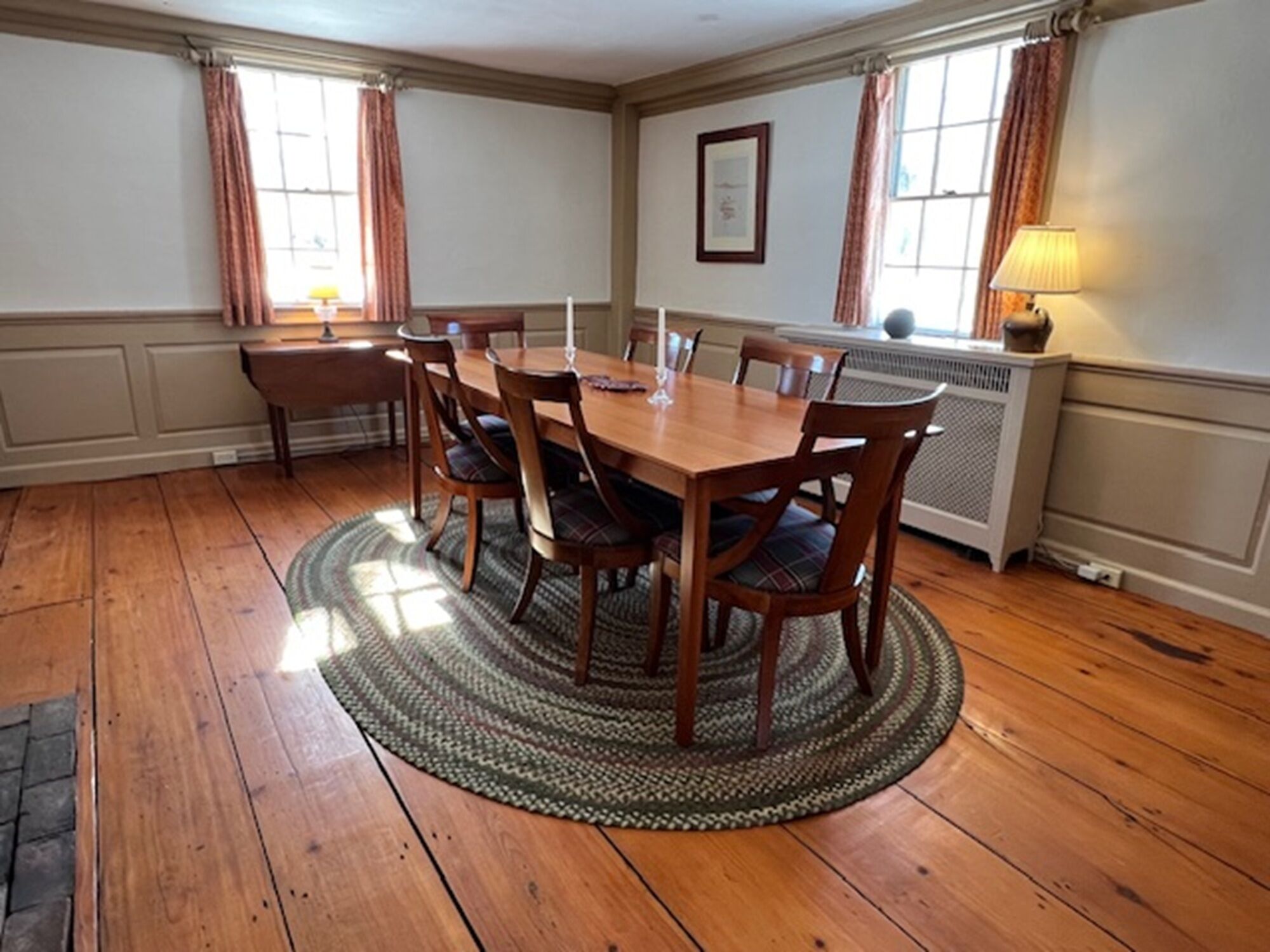 Comedor con mesa y sillas de madera, alfombra estampada y radiador.