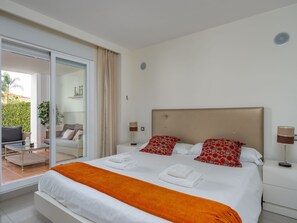 Habitación de hotel moderna con una cama grande, una puerta de cristal que da a un balcón y una decoración en tonos blancos.
