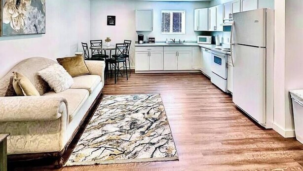 Una cocina moderna con armarios blancos, un comedor con sofá y sillones, y suelo de madera.