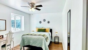 Un dormitorio con cama, escritorio, silla, ventilador de techo y ventana con persianas.