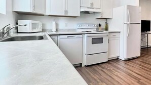 Una cocina moderna con armarios blancos, un lavaplatos de acero inoxidable, un microondas, un horno y un refrigerador.