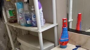 Un baño con lavamanos, espejo y repisas con artículos de aseo.