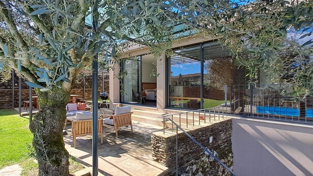 Un patio moderno al aire libre con pared de piedra, mesa de madera y zona de estar con cojines.