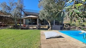 Un patio trasero con piscina, zona de estar cubierta y un muro de piedra.