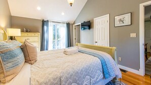 Un dormitorio con cama, mesita de noche, lámpara, televisor y puerta.