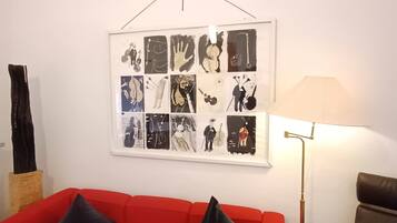 En röd soffa med svarta kuddar, en inramad collagebestående av svartvita bilder på väggen och en golvlampa.