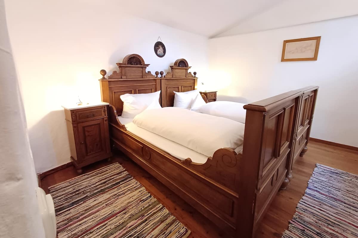 Ein hölzernes Bett mit weißer Bettwäsche, ein Nachttisch, eine Wanduhr und ein gerahmtes Bild.