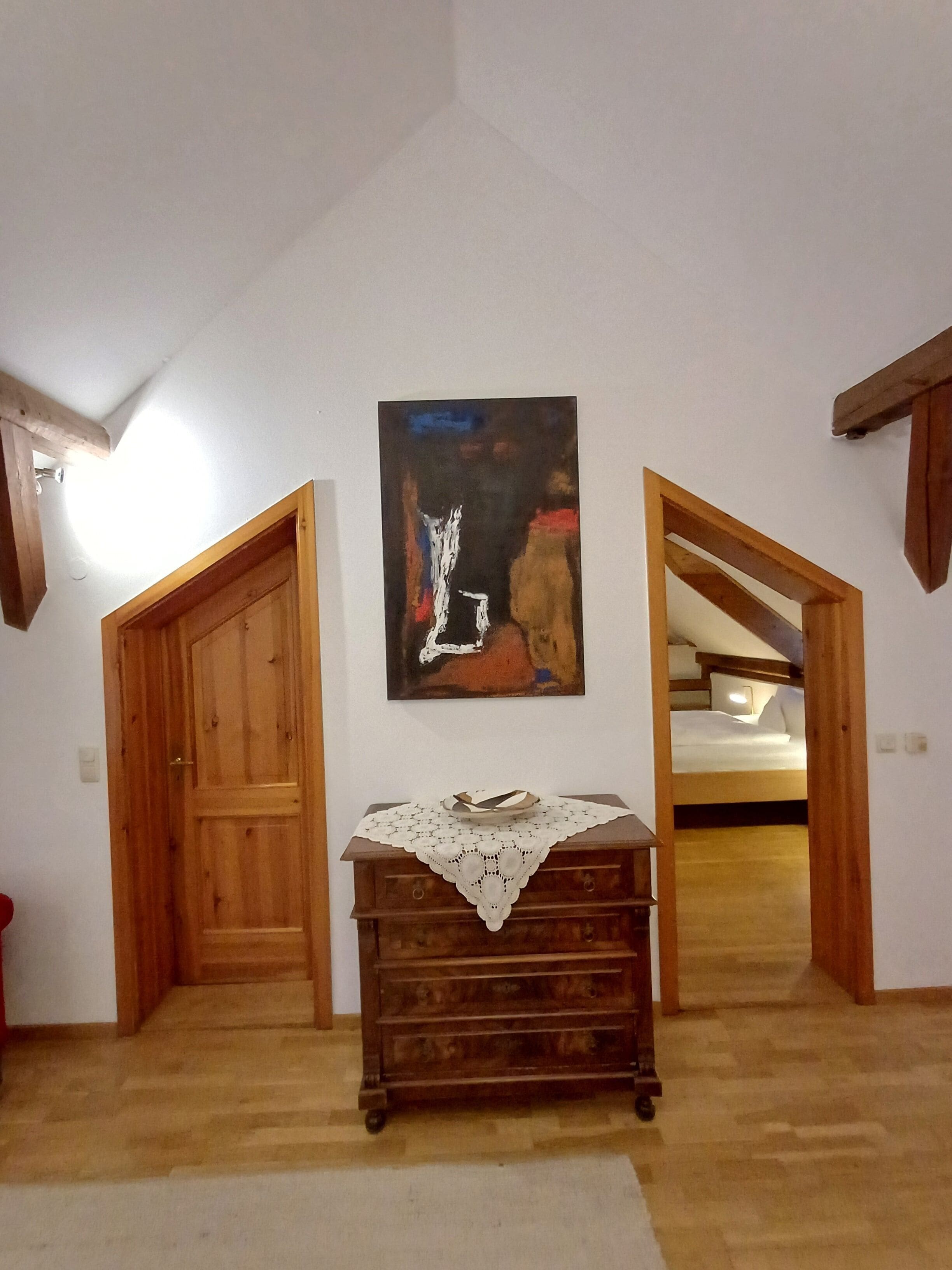 A room with a wooden dresser, a painting on the wall, and a door leading to another room.