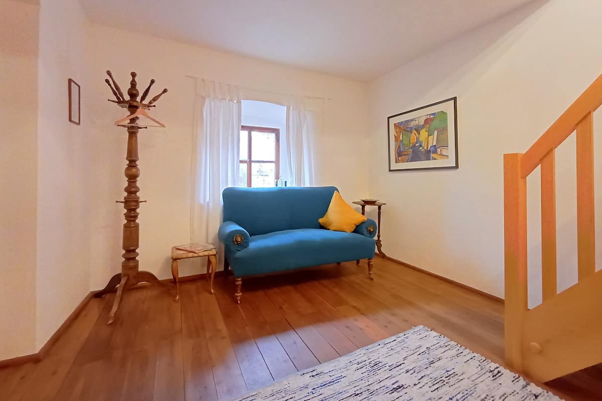Ein Wohnzimmer mit einem blauen Sofa, einem kleinen Beistelltisch, einer hohen Stehlampe, einer Holztreppe und einem Bild an der Wand.