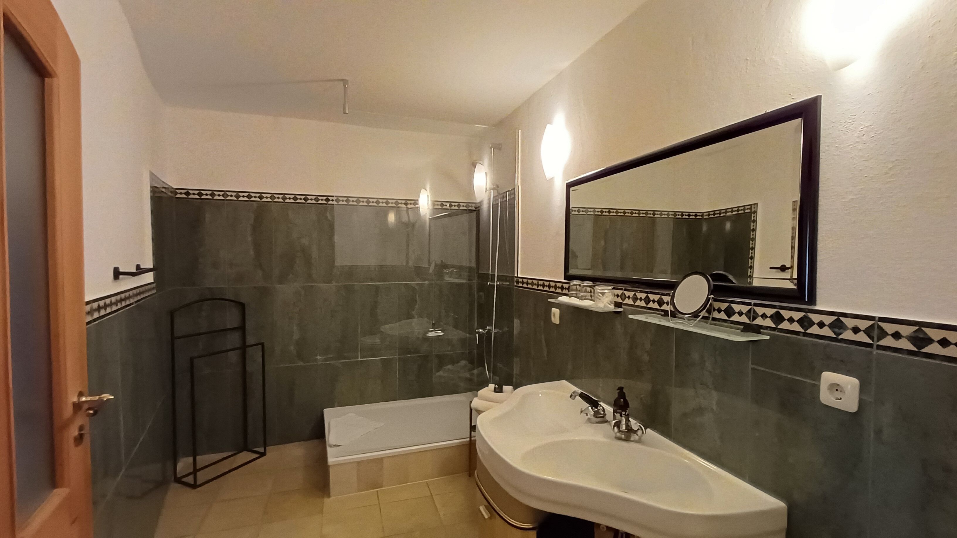 Un bagno con doccia, lavandino, specchio e porta asciugamani.