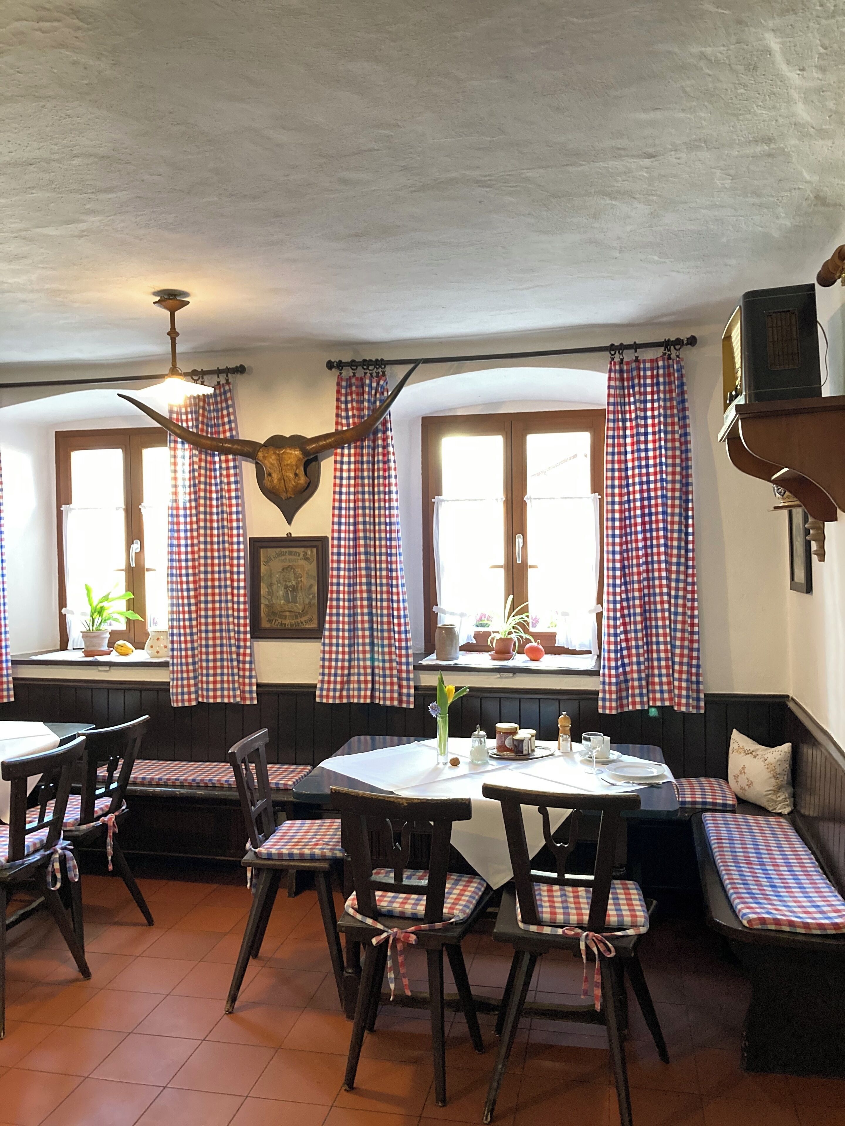 Un comedor con cortinas a cuadros, muebles de madera y techo rústico.